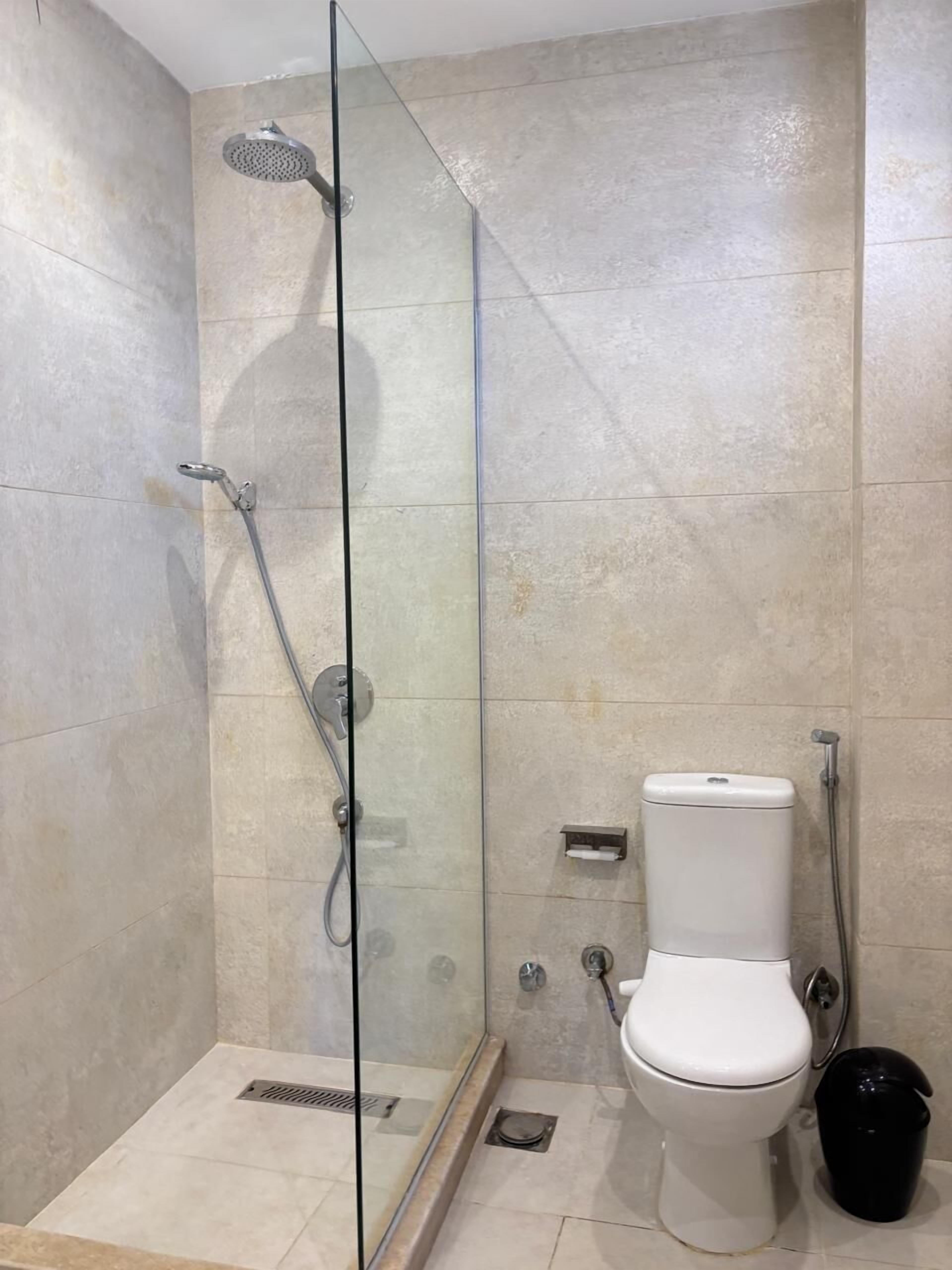 A modern bathroom with a glass-enclosed shower, a toilet, and a black trash bin.