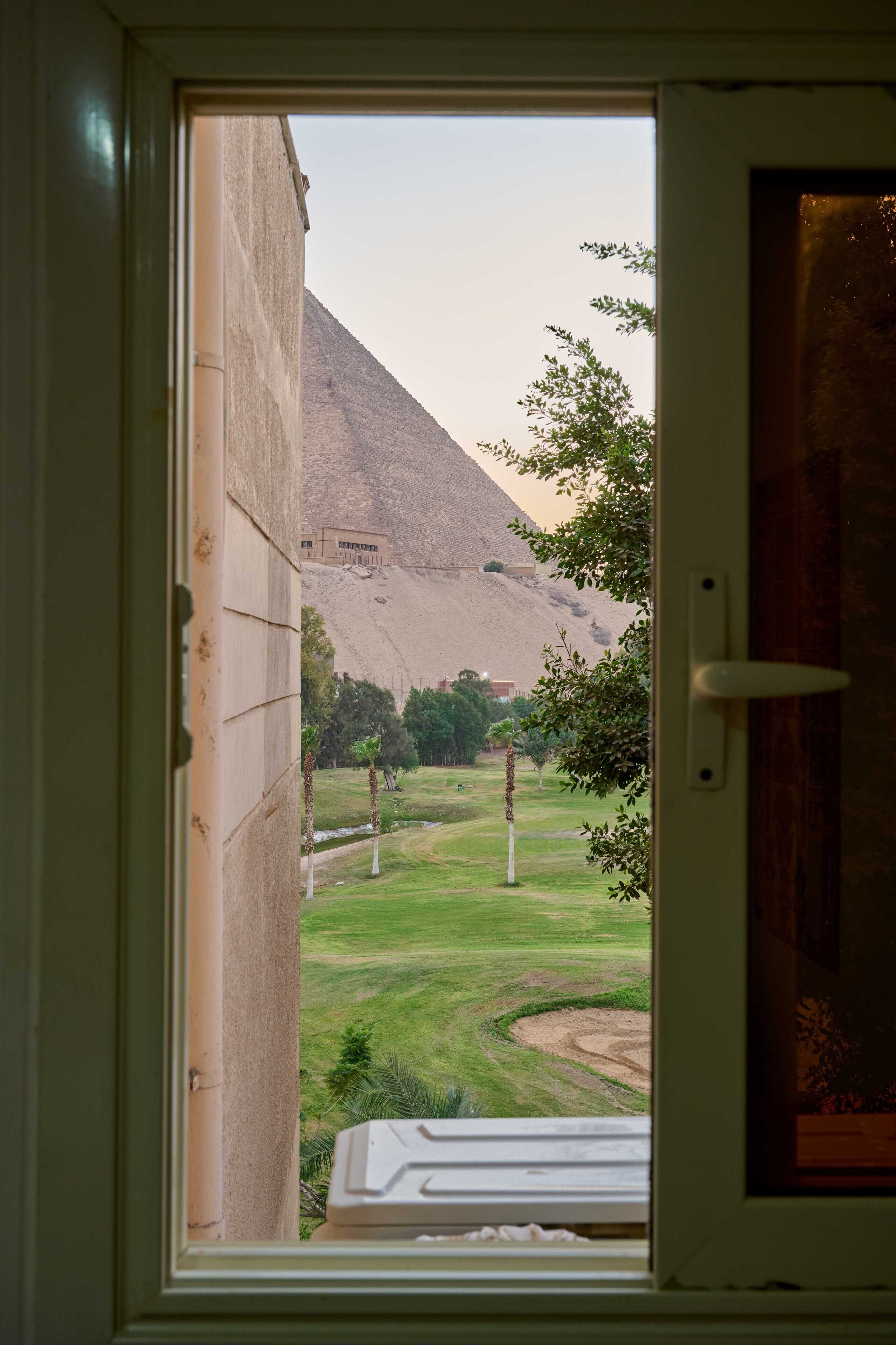 Une vue à travers une fenêtre donnant sur une pyramide et une zone herbeuse.