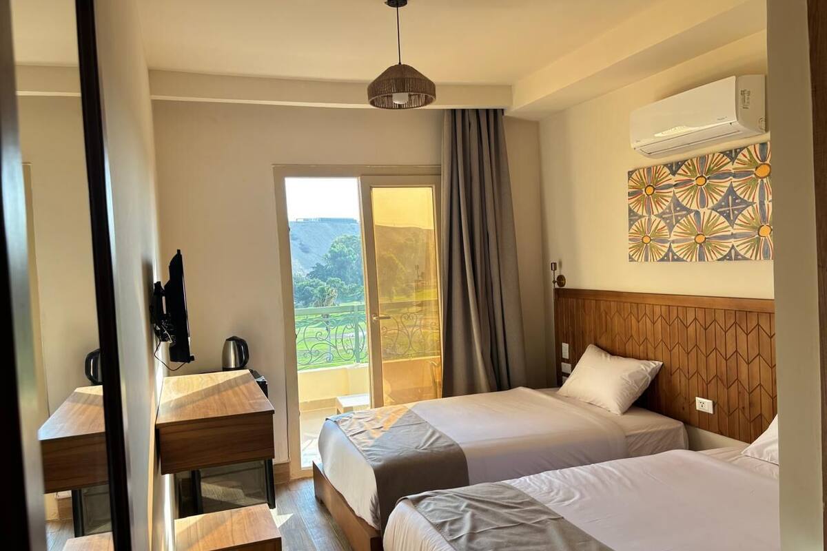 Una habitación de hotel con dos camas, un escritorio de madera, una computadora portátil y un aire acondicionado.