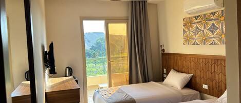 A hotel room with two beds, a wooden desk, a laptop, and an air conditioner.
