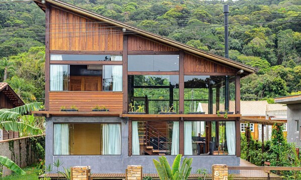 A modern two-story house with a wooden exterior, large windows, and a balcony. - 3BR Duplex w/ BBQ & Garage Near Beach Emb686 (Bombinhas)