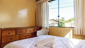 A bedroom with a bed, a wooden dresser, a window with curtains, and a view of the outside. - 3BR Duplex w/ BBQ & Garage Near Beach Emb686 (Bombinhas)
