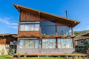 A modern two-story house with a wooden facade, large windows, and a visible chimney.