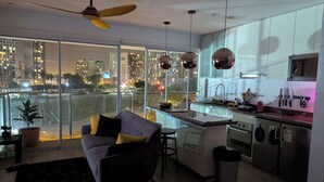 A modern kitchen with a large island, a dining area with a sofa, and a view of a cityscape at night. - Beautiful  loft in Barranco (Barranco)