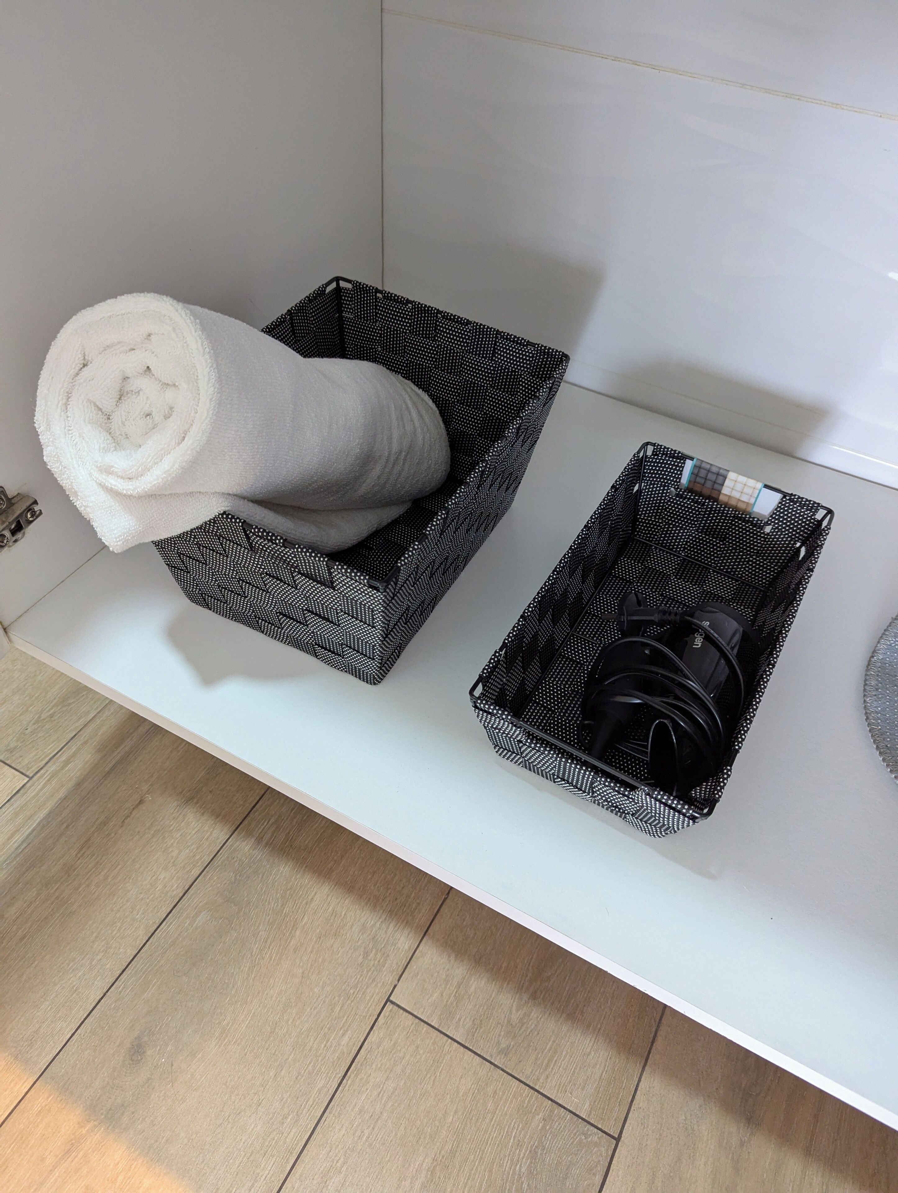 A white bathroom with two black and white patterned baskets on a white countertop.