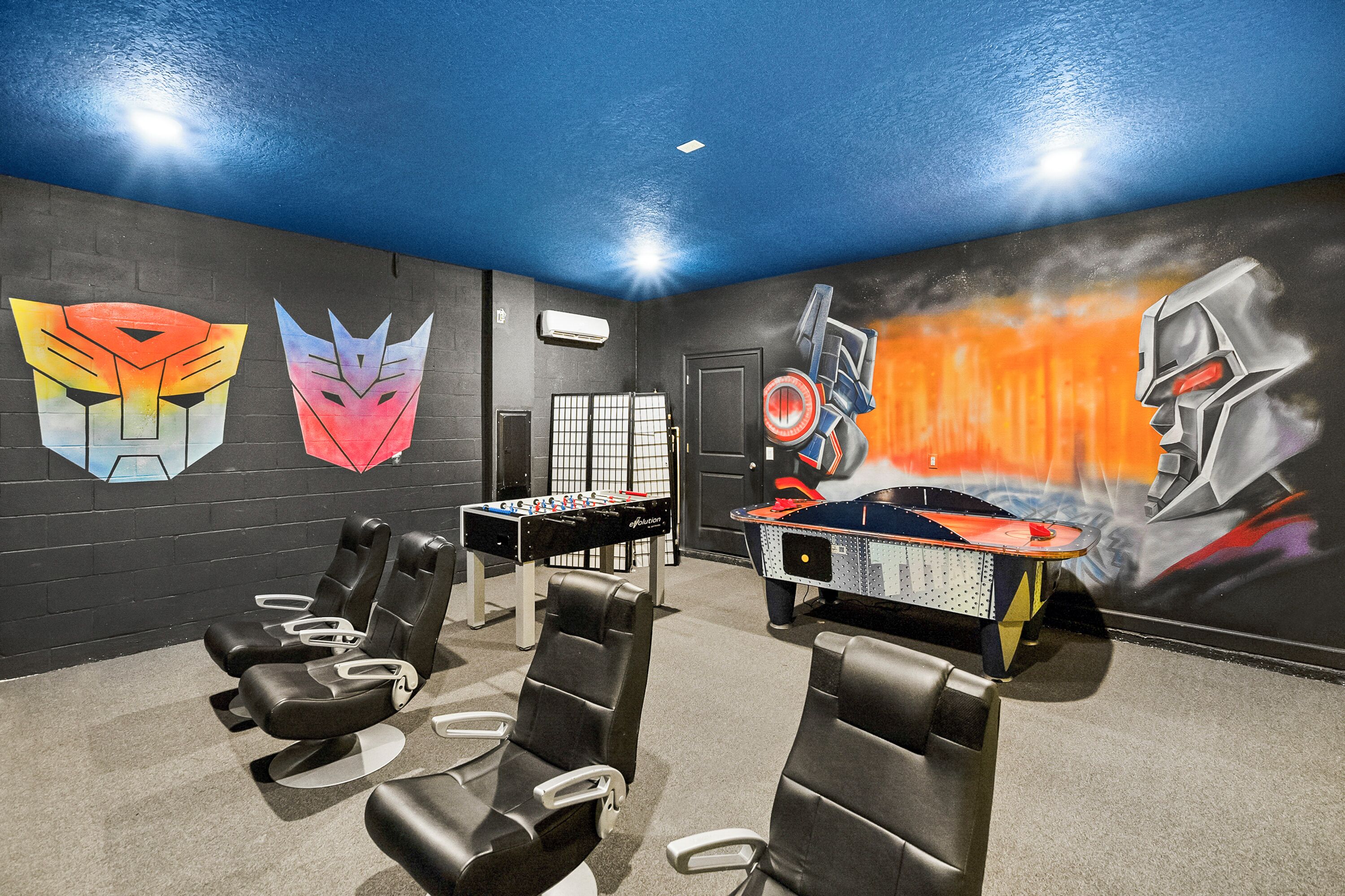 A room with four massage chairs, a foosball table, and a wall mural.