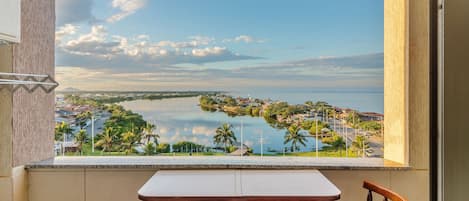 A balcony with a table and chairs, overlooking a calm lake and a distant town.