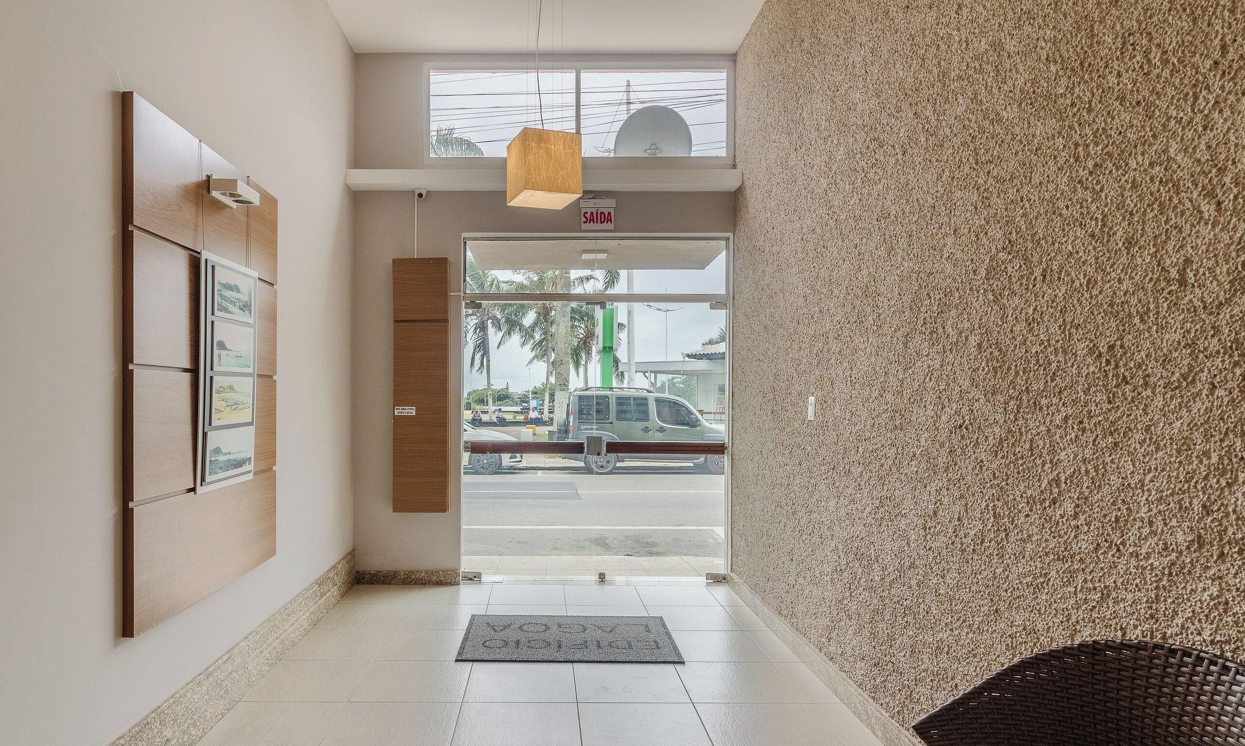 Entrada de un hotel con piso de baldosas, un mostrador de recepción, cuadros enmarcados en la pared y vista de la calle.