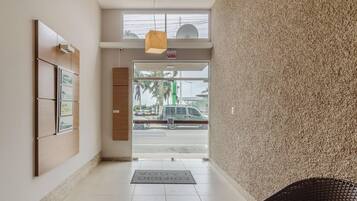 Entrada de un hotel con piso de baldosas, un mostrador de recepción, cuadros enmarcados en la pared y vista de la calle.