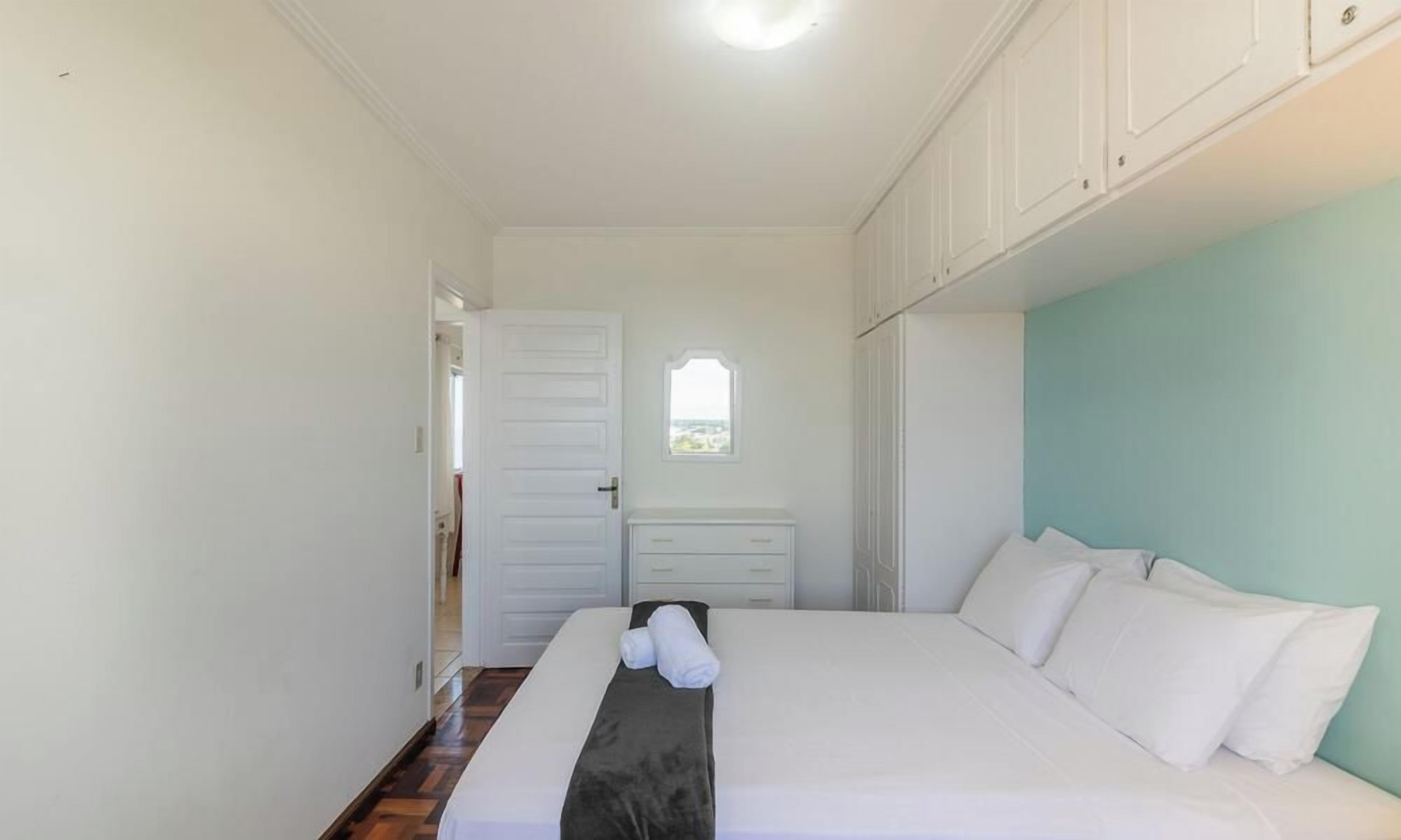 A bedroom with a bed, a nightstand, a window, and a door.