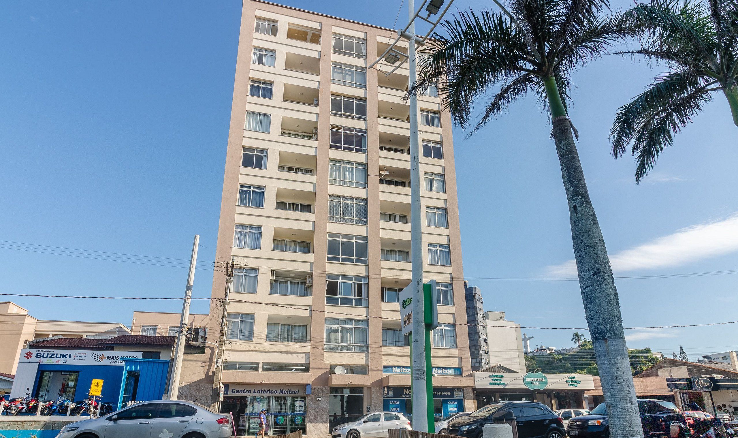 A multi-story building with balconies, a visible clock, and various storefronts including a Suzuki dealership.