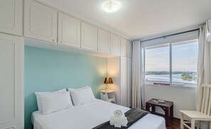 A hotel room with a bed, a nightstand with a lamp, a chair, and a view of the water. - Stay With an Ocean View! Elg0071 (Barra Velha)