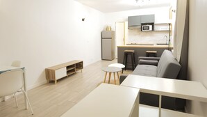 Ein kompakter Wohnbereich mit Küchenzeile, einer Couch, einem Esstisch und einer kleinen Sitzecke.