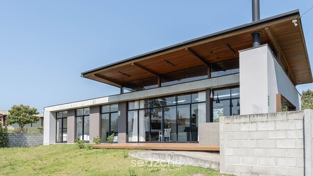 A modern house with large windows, a wooden roof, and a chimney. - Comfortable House Near Praia do Rosa Egi001 (Imbituba)