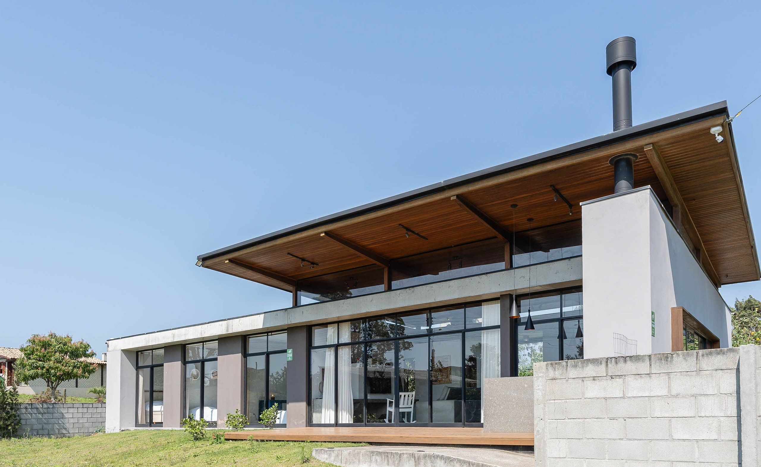 A modern house with large windows, a wooden roof, and a chimney.