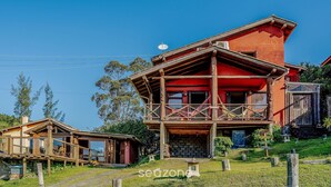 Ein zweistöckiges Holzhaus mit Balkon, Satellitenschüssel und einer kleinen Gartenhütte im Vordergrund.