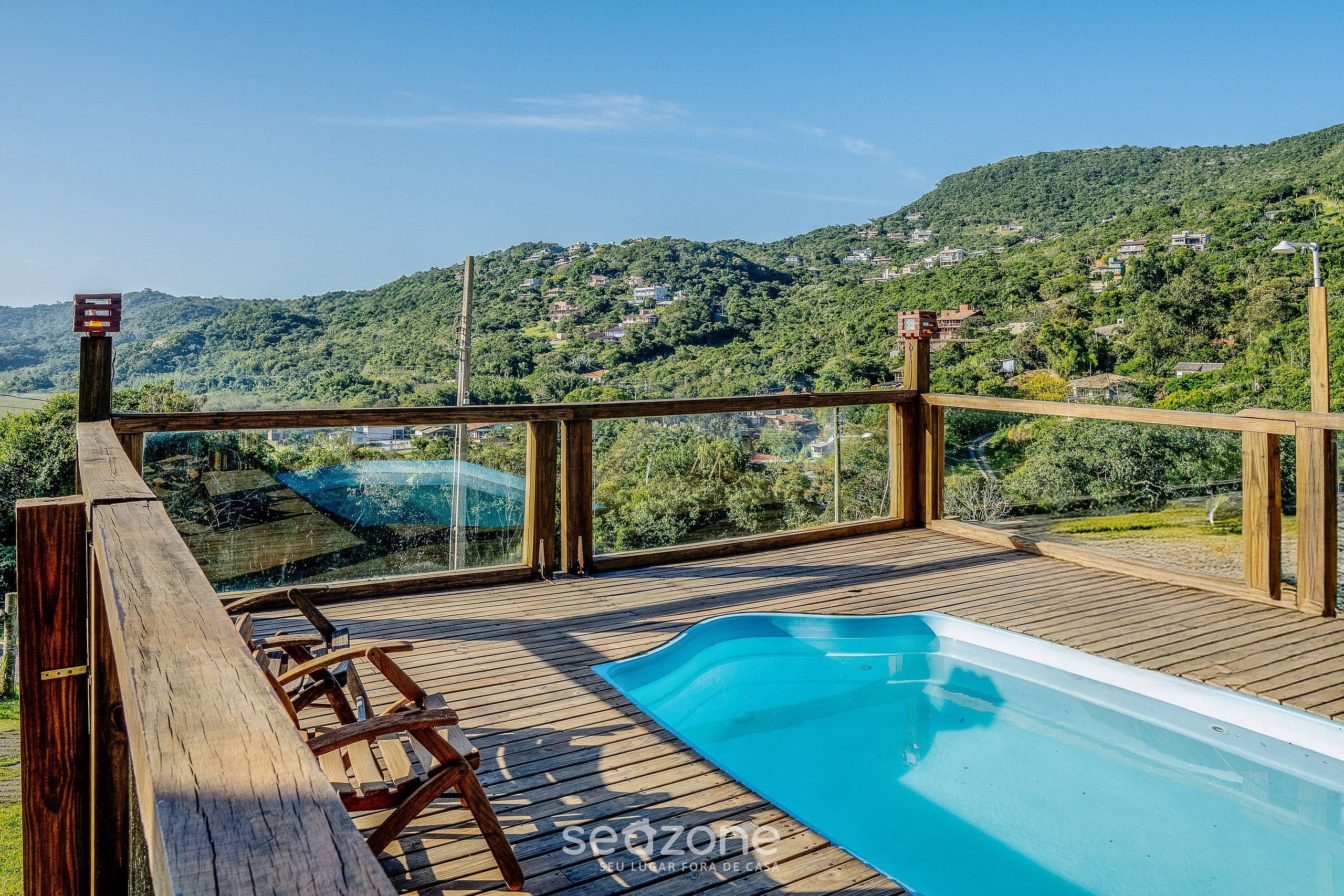 Una terraza de madera con piscina, con vistas a una colina con casas.