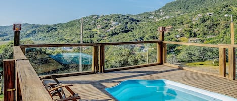 Una terraza de madera con piscina, con vistas a una colina con casas.