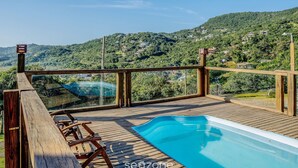 Eine Holzterrasse mit Swimmingpool mit Blick auf eine Hügelslandschaft mit Häusern.