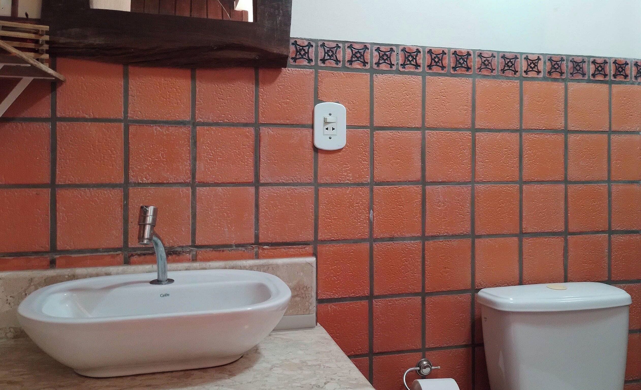 Une salle de bain avec un lavabo blanc, des toilettes et un mur recouvert de carreaux agrémenté d’une bordure décorative.