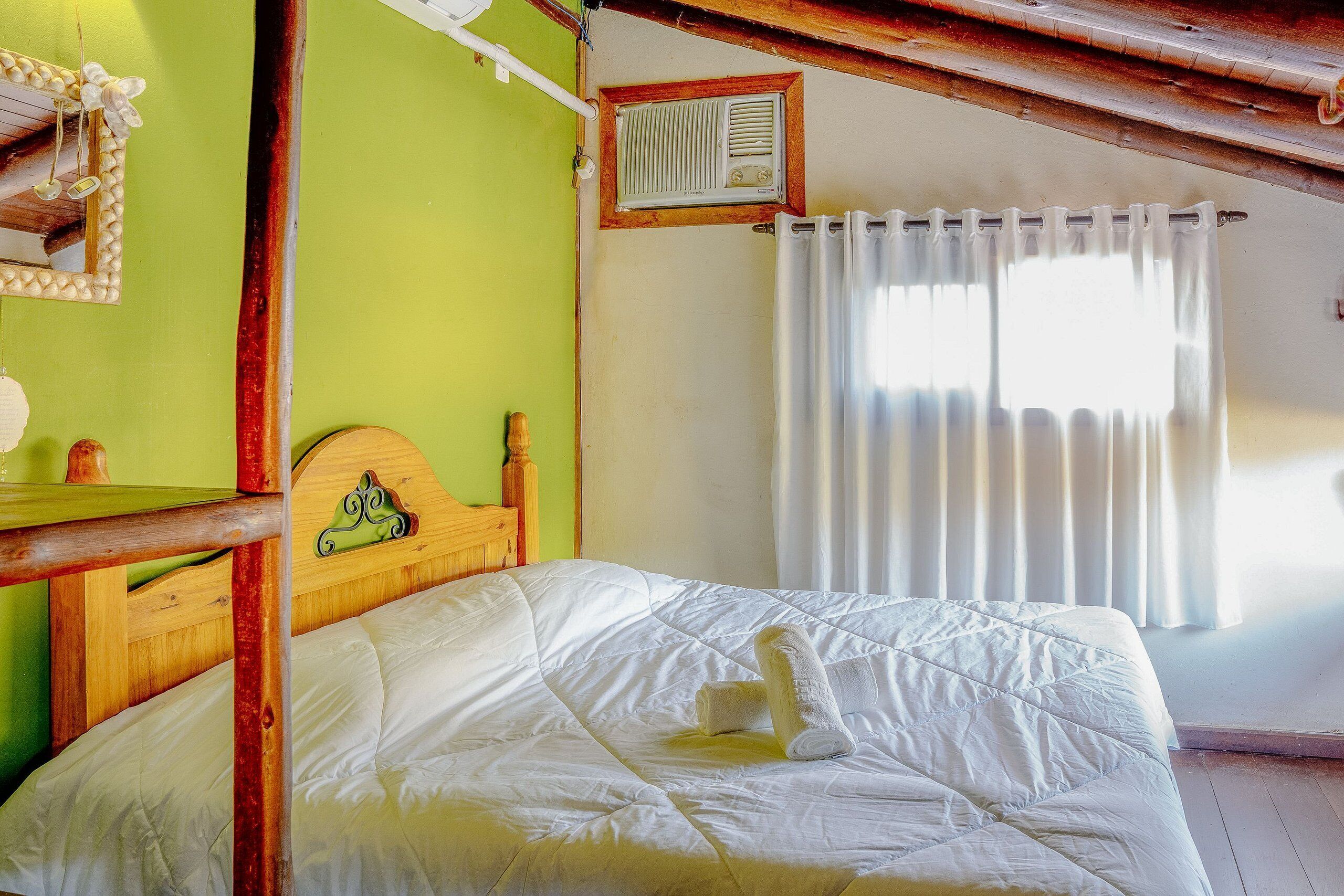 Une pièce avec un lit en bois, une petite table, un miroir et une fenêtre avec des rideaux.