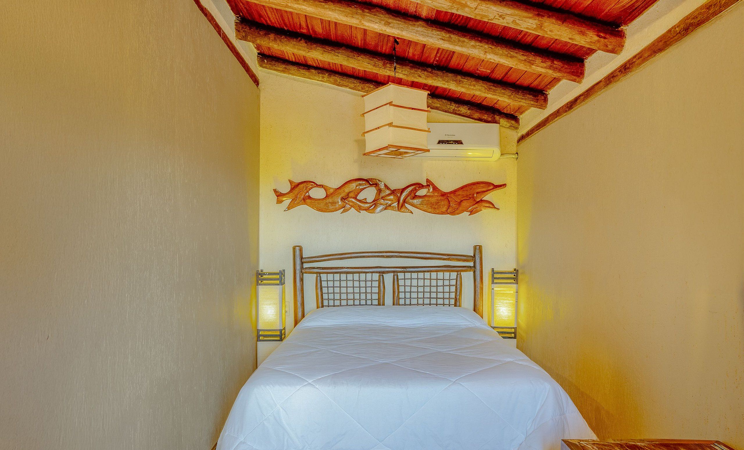 Quarto de hotel com cama, vigas de madeira no teto, ar condicionado fixado na parede e arte decorativa.