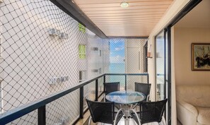 Un balcón con una mesa y sillas de vidrio, una cerca de alambre y un edificio al fondo.