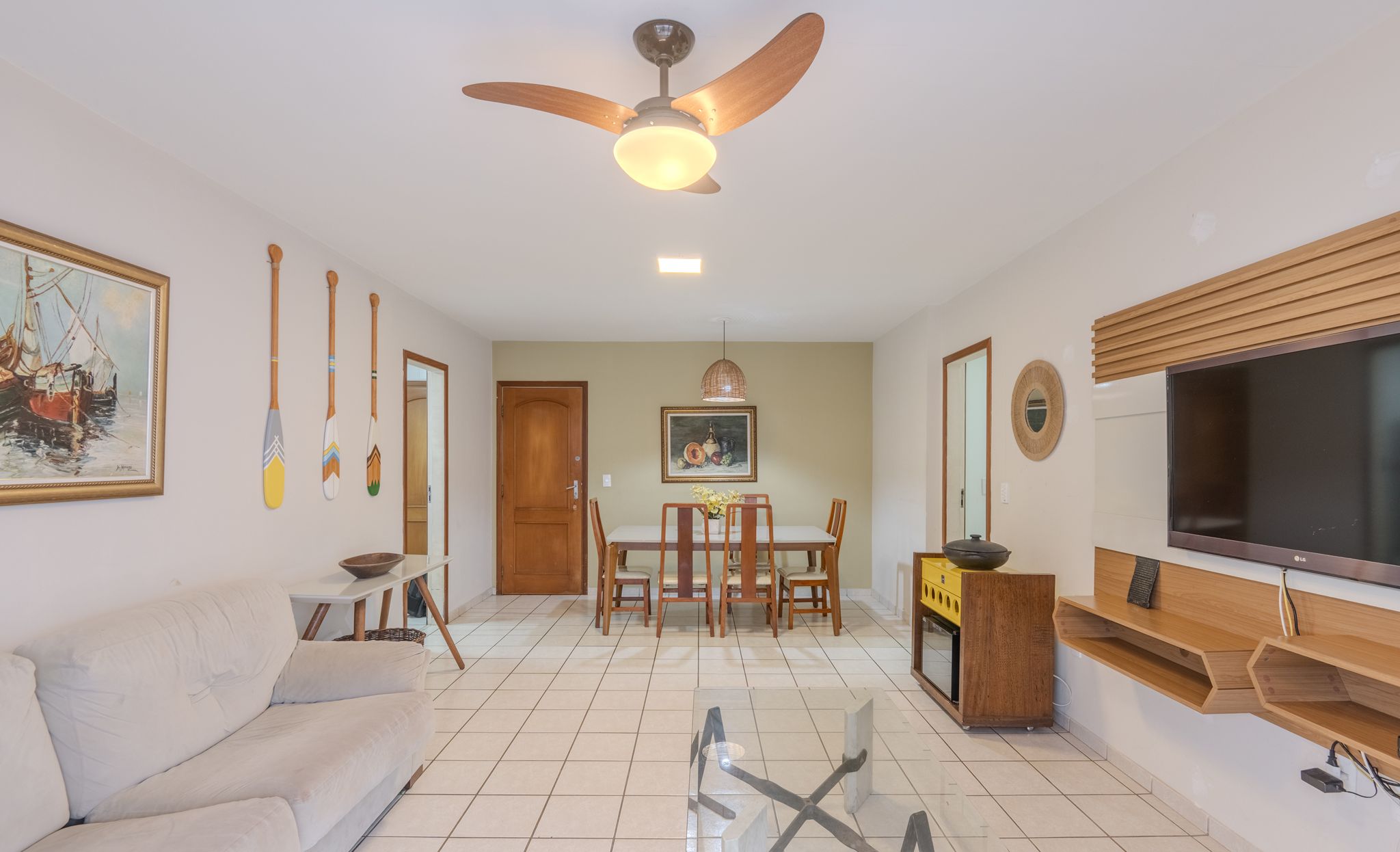 A living room with a sofa, a dining table with chairs, a ceiling fan, a TV, and a painting on the wall.