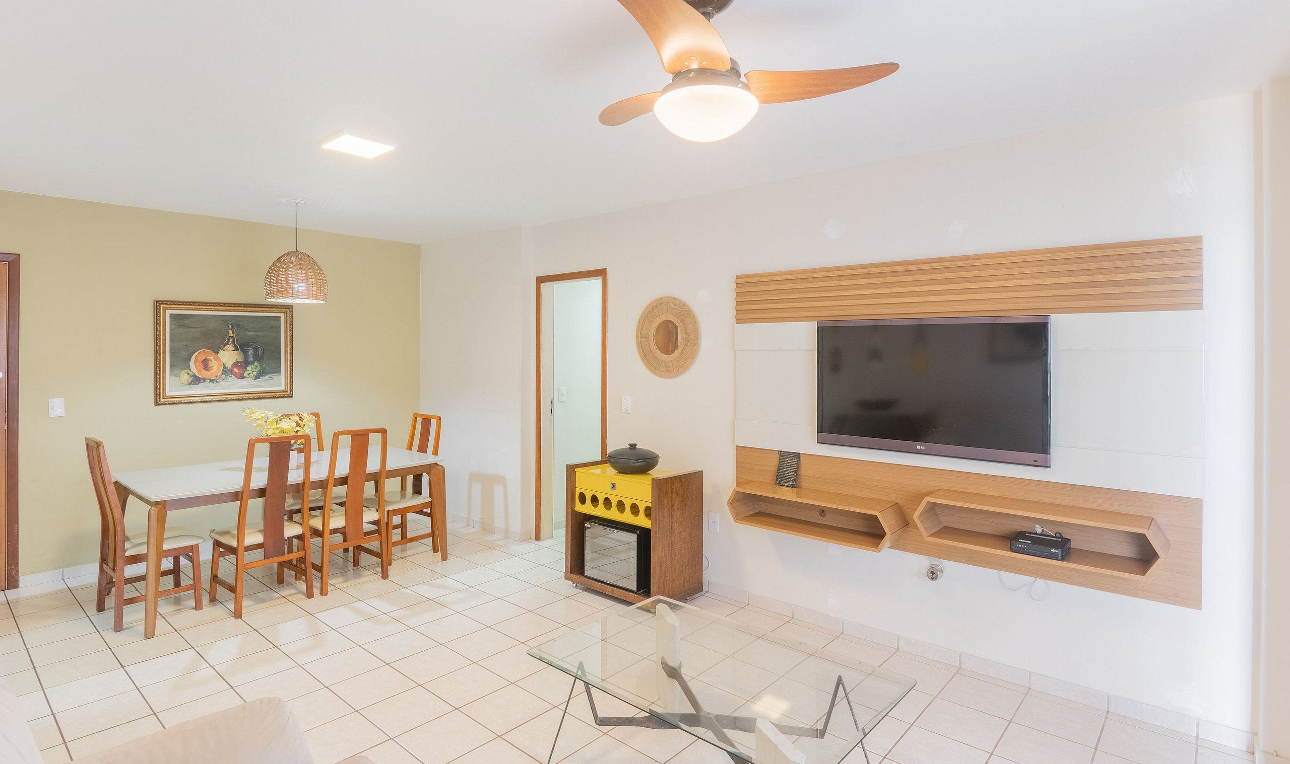 A living room with a dining area, a ceiling fan, a flat-screen TV, and a small wooden cabinet.