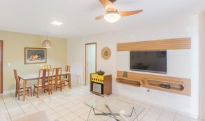 A living room with a dining area, a ceiling fan, a flat-screen TV, and a small wooden cabinet. - Apartment in a Condominium on the Sand - Efe0803 (Guarapari)