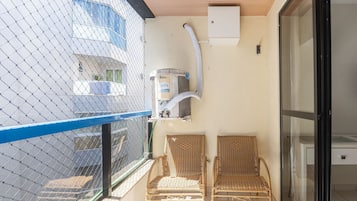 A balcony with two wicker chairs, a ceiling fan, and a wall-mounted air conditioning unit.