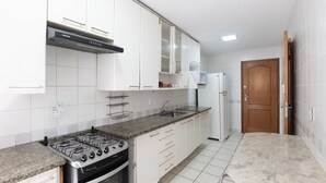 Una cucina con mobili bianchi, un fornello a gas, forno integrato, lavello e frigorifero.