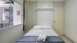 Un dormitorio con una cama, una ventana, un armario y una toalla sobre la cama.