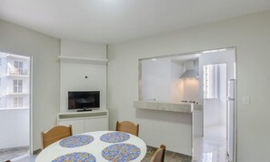 Une pièce comprenant une table ronde, des chaises, un téléviseur, un coin cuisine avec une cuisinière et une porte donnant sur une autre pièce.