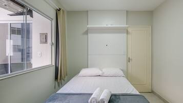 Een slaapkamer met een bed, een raam, een kast en een handdoek op het bed.