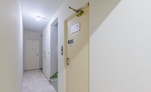 Un couloir étroit avec une porte blanche sur la droite, un interrupteur et une petite fenêtre.