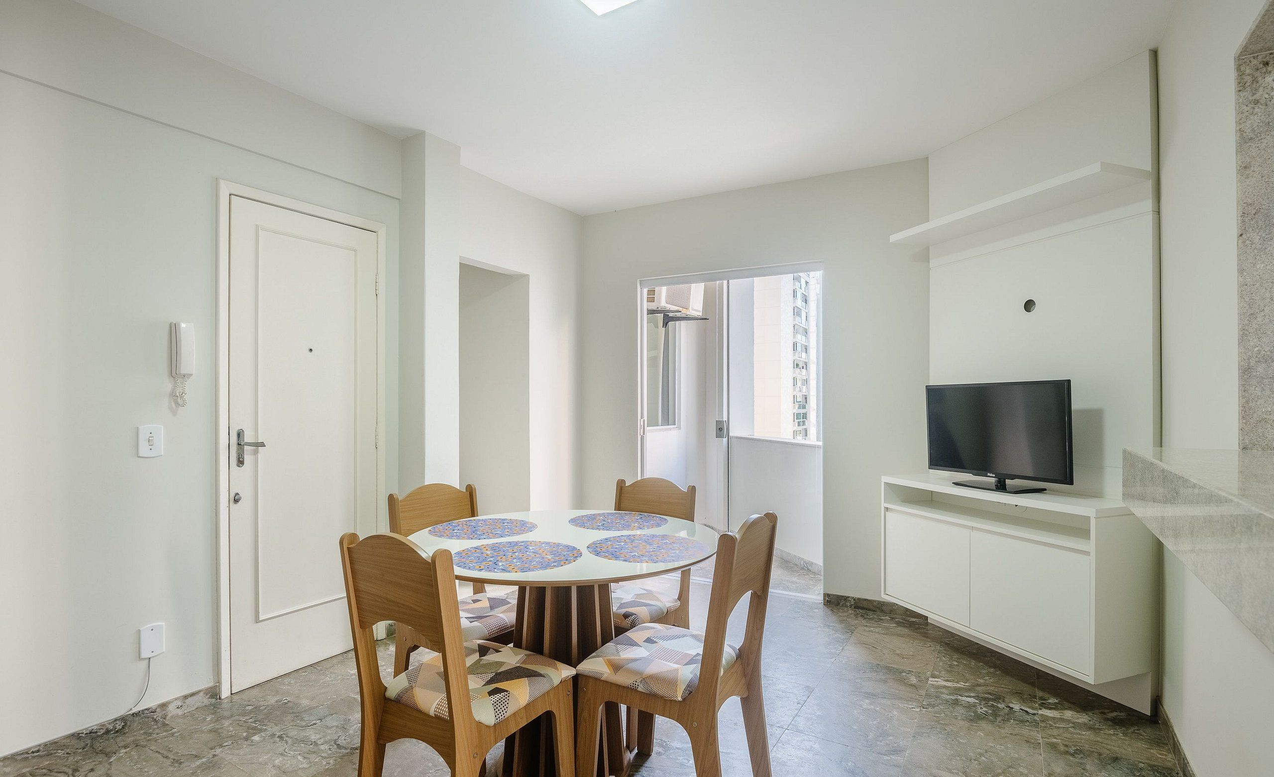 A dining area with a round table, chairs, a TV, and a white cabinet.