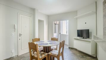 A dining area with a round table, chairs, a TV, and a white cabinet.