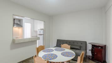 A compact living space with a dining table, chairs, a sofa, and a small kitchen area.