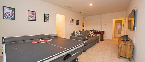 Una sala de estar con mesa de ping pong, sofá y televisor.