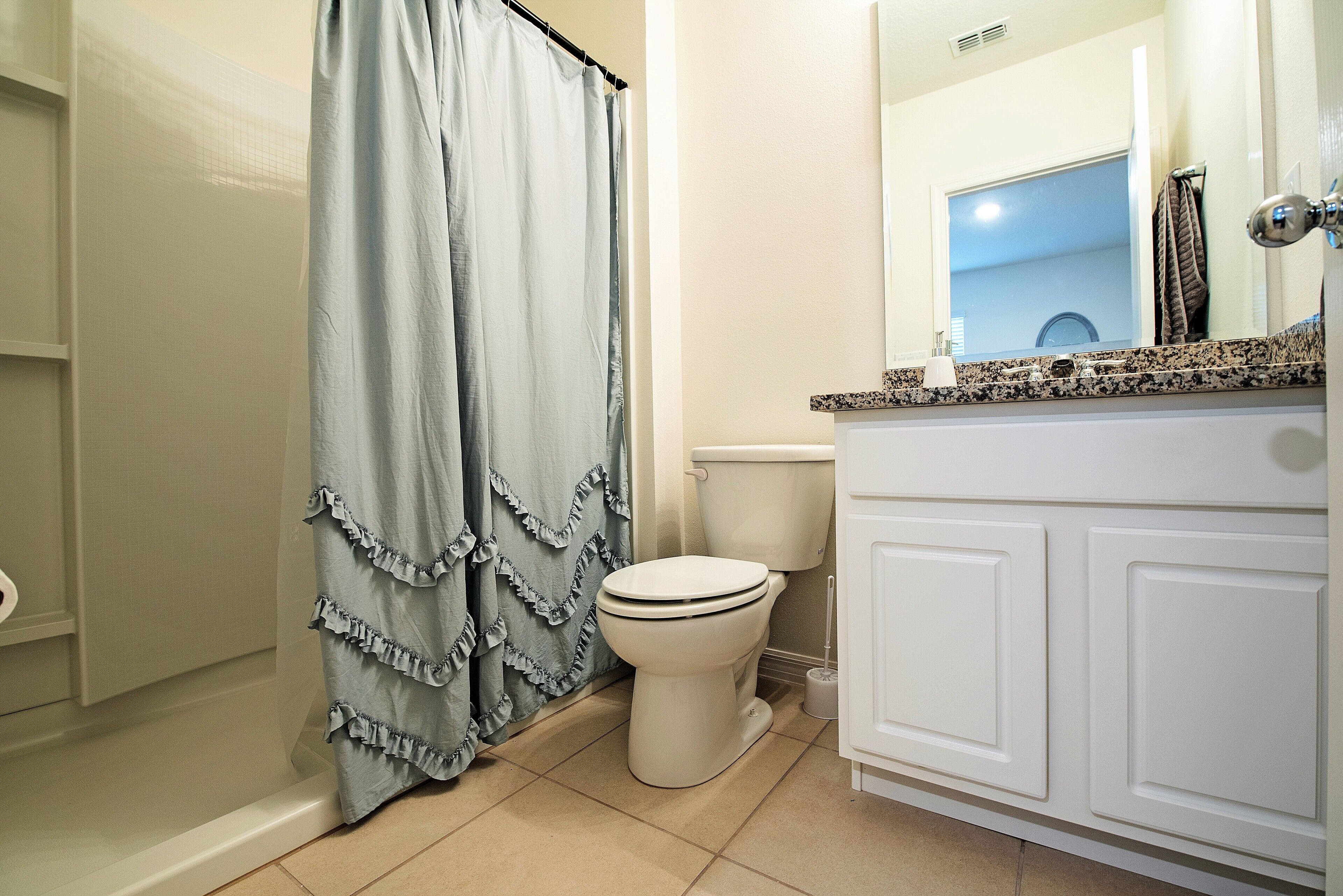 Un baño con inodoro, cortina de ducha y tocador con espejo.