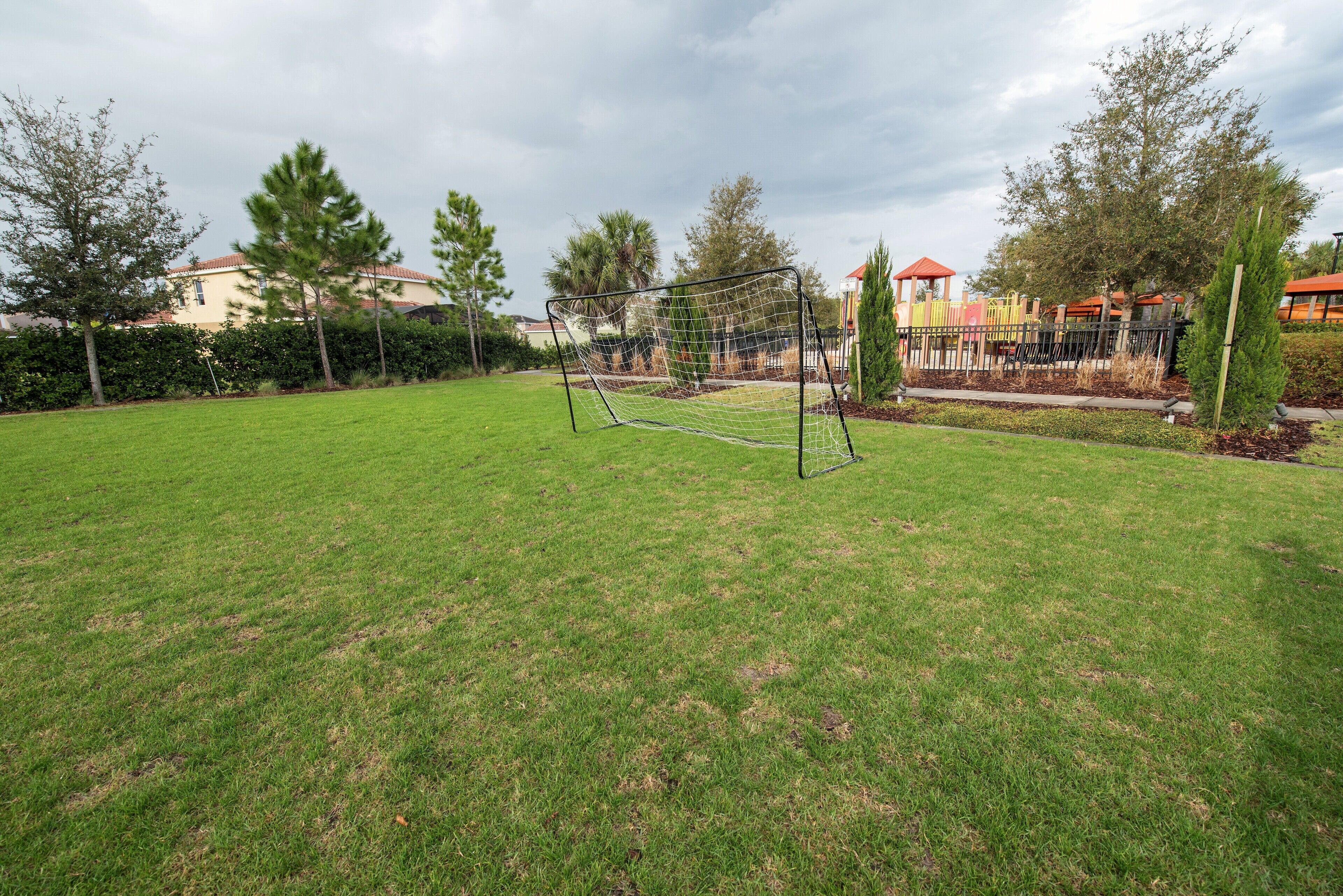 Een gazon met een voetbaldoel, bomen en een speeltuin op de achtergrond.