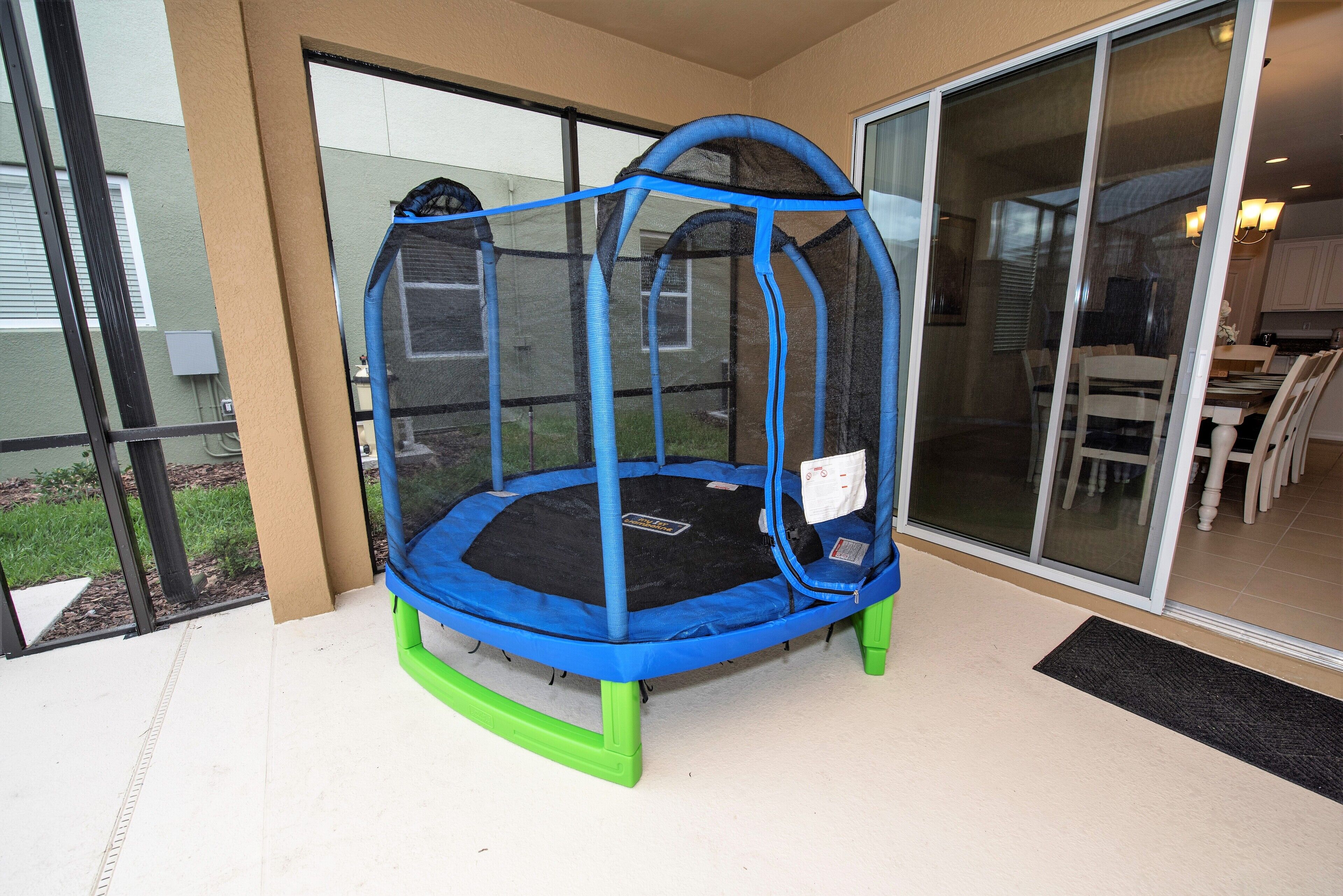 A trampoline with a safety net, green legs, and a black jumping surface, located indoors near a sliding glass door.