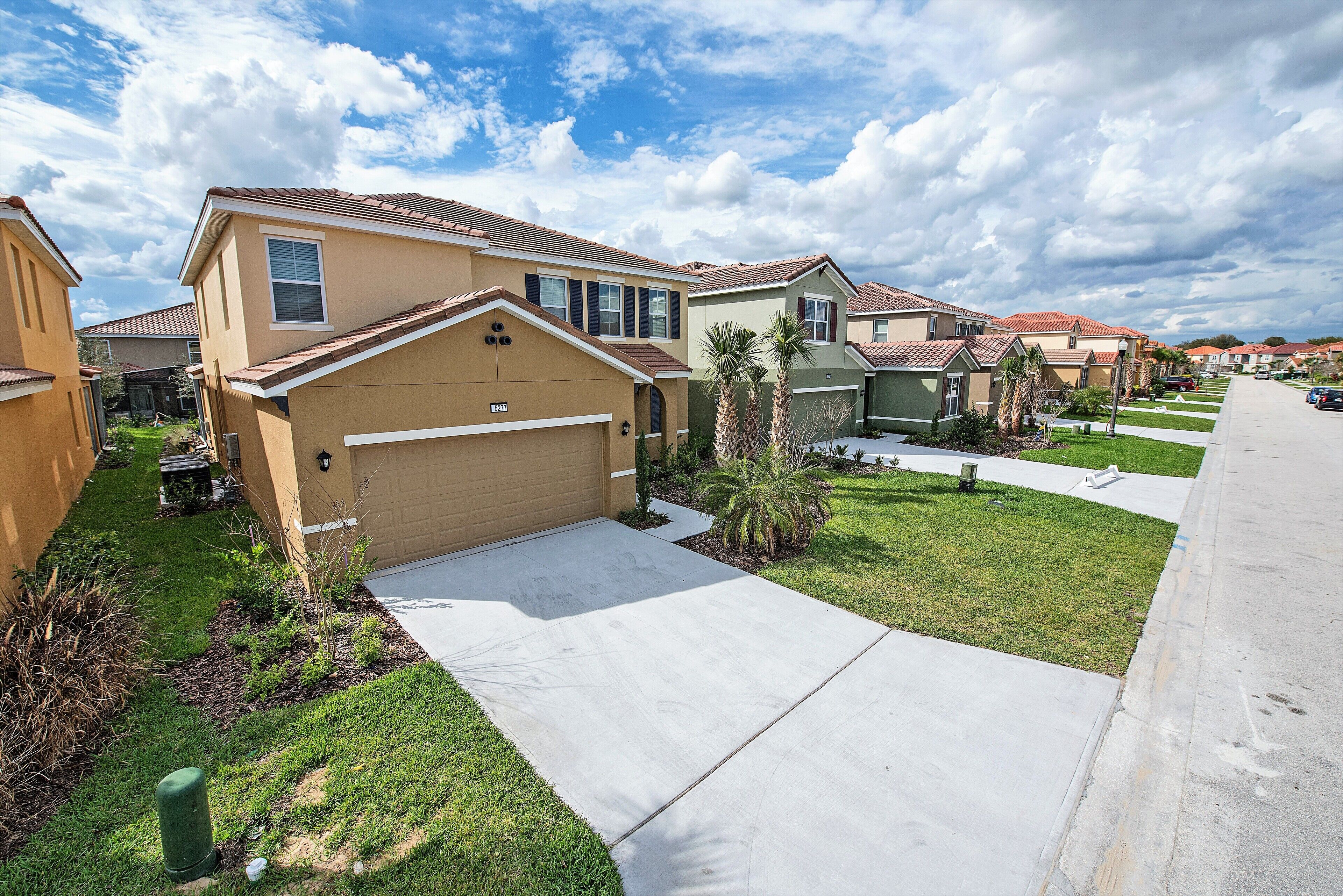 A residential neighborhood with single-family homes, a clear sky, and a well-maintained lawn.