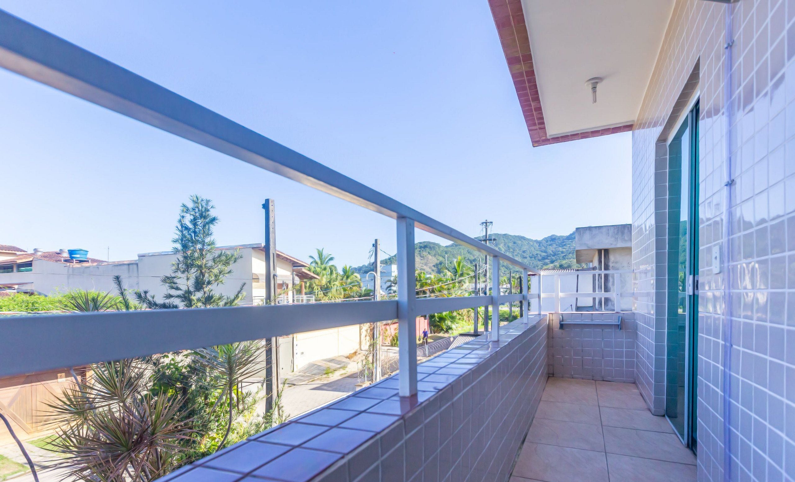 A balcony with a view of a residential area, a tiled wall, and a door.