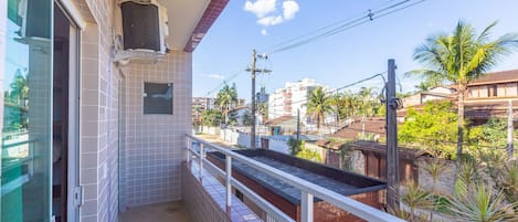 A narrow balcony with tiled walls, a small window, and a view of a residential area with buildings and palm trees.
