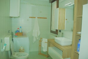 A bathroom with a toilet, sink, and mirror. There are towels hanging on a rack and a basket of toiletries on the sink.