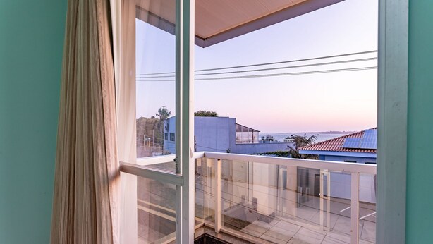 Un balcone con ringhiera in vetro, vista sul mare e un edificio con tetto blu sullo sfondo.