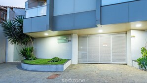 Un edificio moderno con facciata rivestita di piastrelle, un portone del garage chiuso e un piccolo spazio verde con piante.