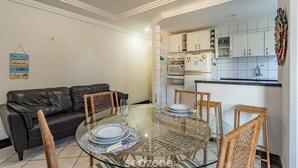 Un soggiorno con tavolo da pranzo in vetro, divano in pelle nera, poltrone in vimini e una cucina con pensili bianchi e un forno a microonde.